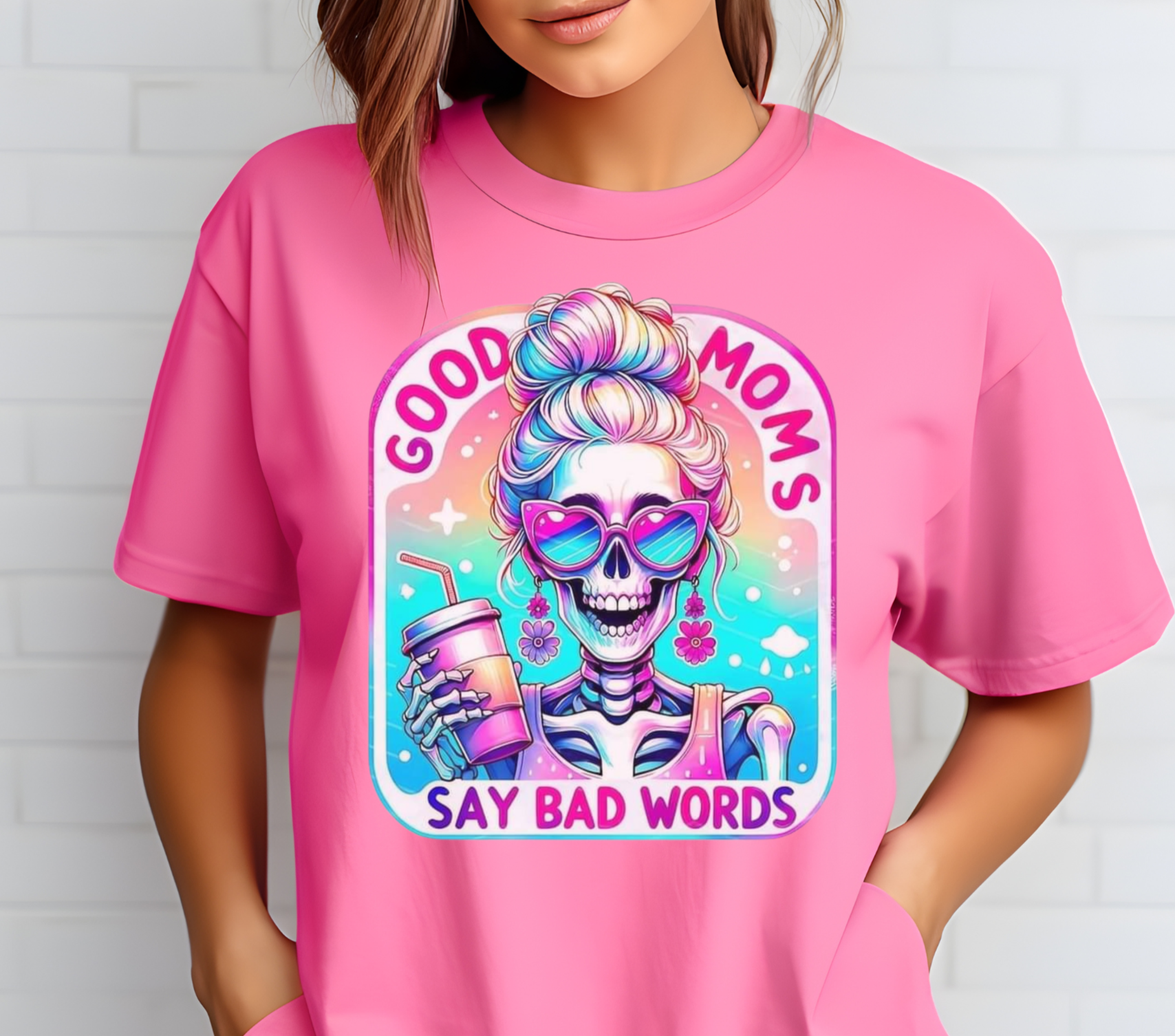 Good Moms Say Bad Words Messy Bun Colorful Skeleton Iced Coffee Shirt. Features a vibrant, retro-style graphic of a skeleton with a messy bun holding an iced coffee, with the text 'Good Moms Say Bad Words.' Soft cotton material in a unisex fit, available in multiple colors. Ideal for casual wear and making a fun, playful statement. Machine washable for easy care.