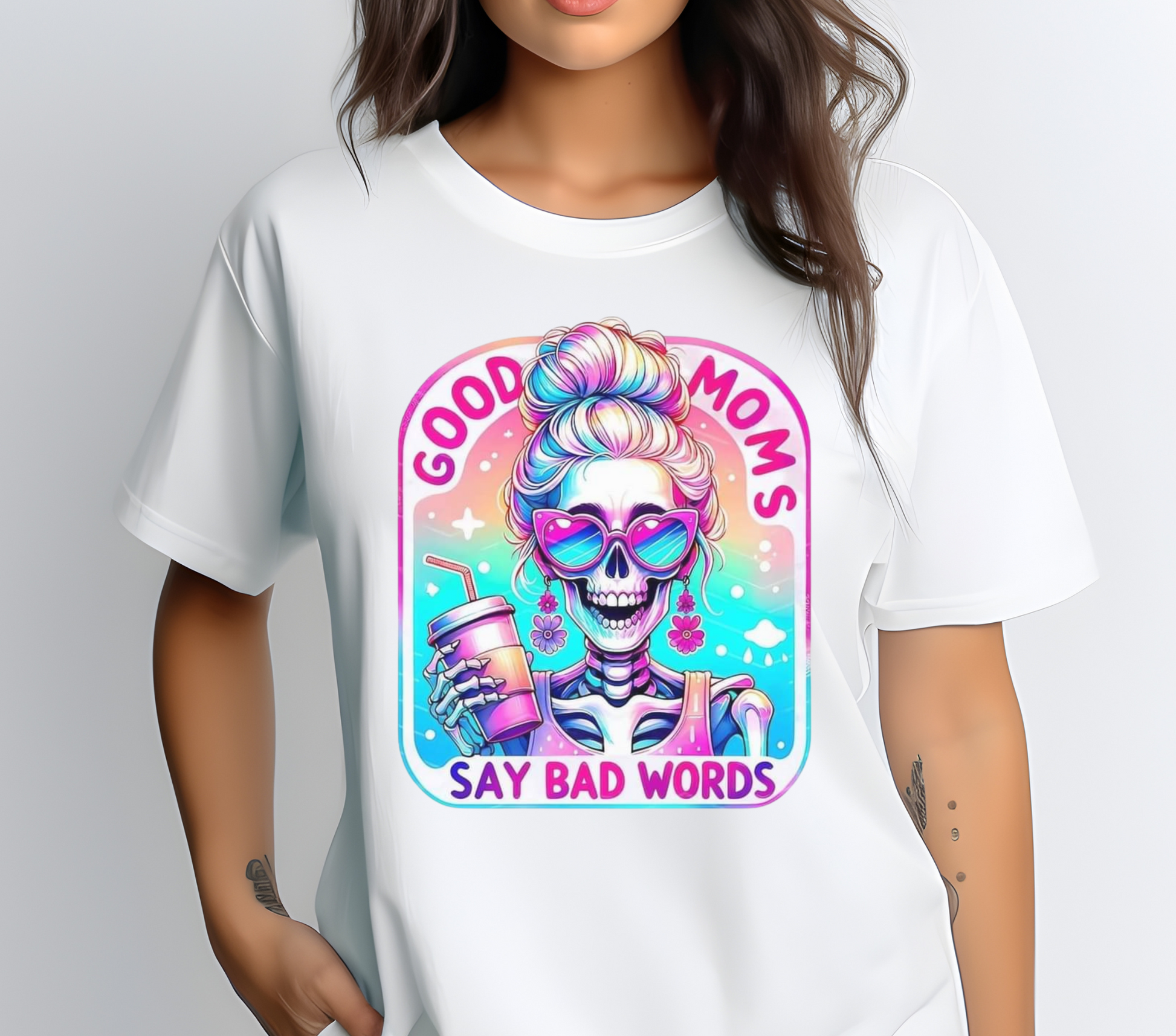 Good Moms Say Bad Words Messy Bun Colorful Skeleton Iced Coffee Shirt. Features a vibrant, retro-style graphic of a skeleton with a messy bun holding an iced coffee, with the text 'Good Moms Say Bad Words.' Soft cotton material in a unisex fit, available in multiple colors. Ideal for casual wear and making a fun, playful statement. Machine washable for easy care.