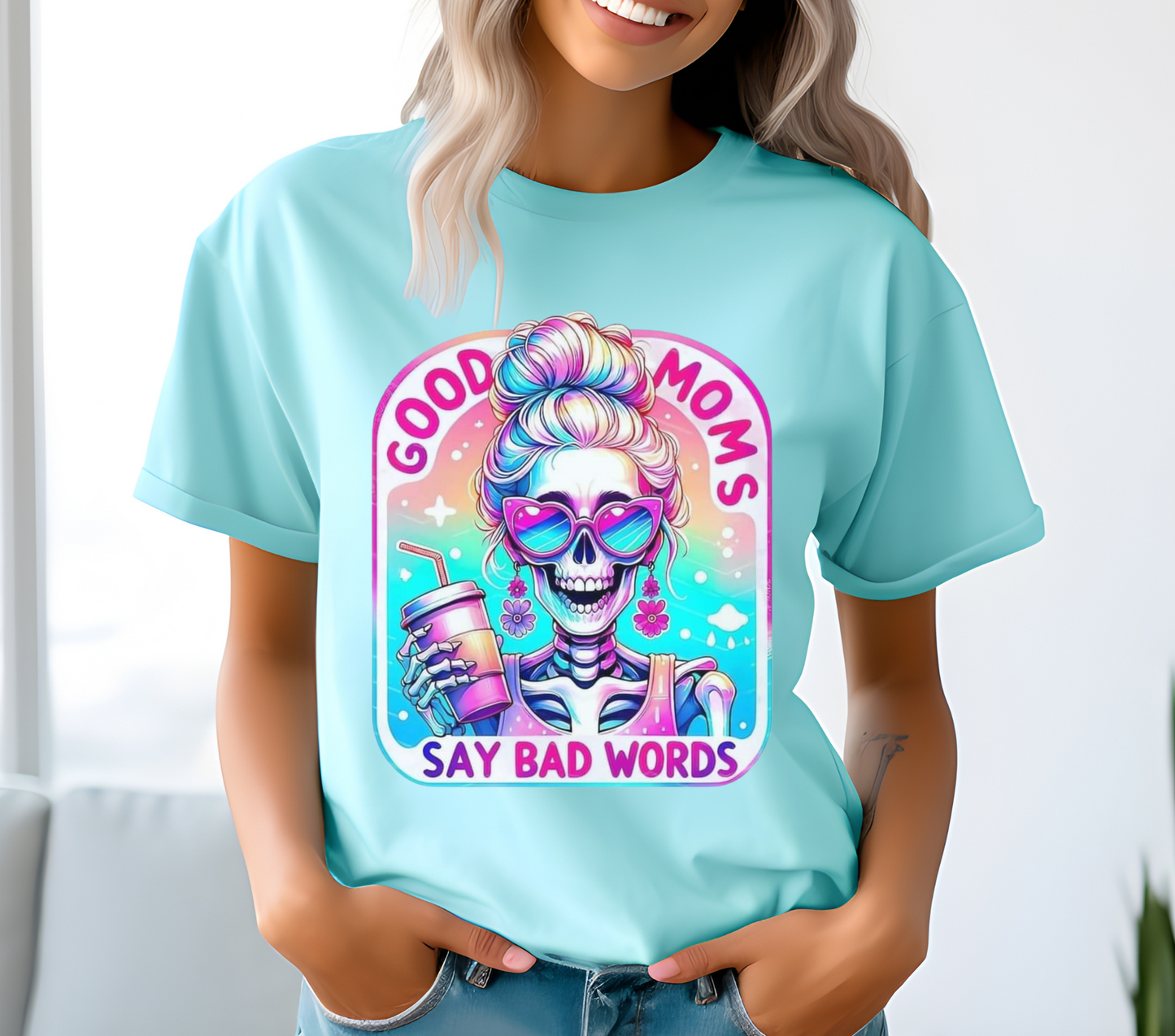 Good Moms Say Bad Words Messy Bun Colorful Skeleton Iced Coffee Shirt. Features a vibrant, retro-style graphic of a skeleton with a messy bun holding an iced coffee, with the text 'Good Moms Say Bad Words.' Soft cotton material in a unisex fit, available in multiple colors. Ideal for casual wear and making a fun, playful statement. Machine washable for easy care.