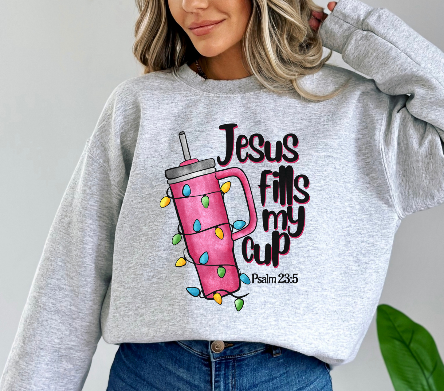 Light pink sweatshirt featuring a tumbler wrapped in Christmas lights with the text “Jesus Fills My Cup” and Psalm 23:5